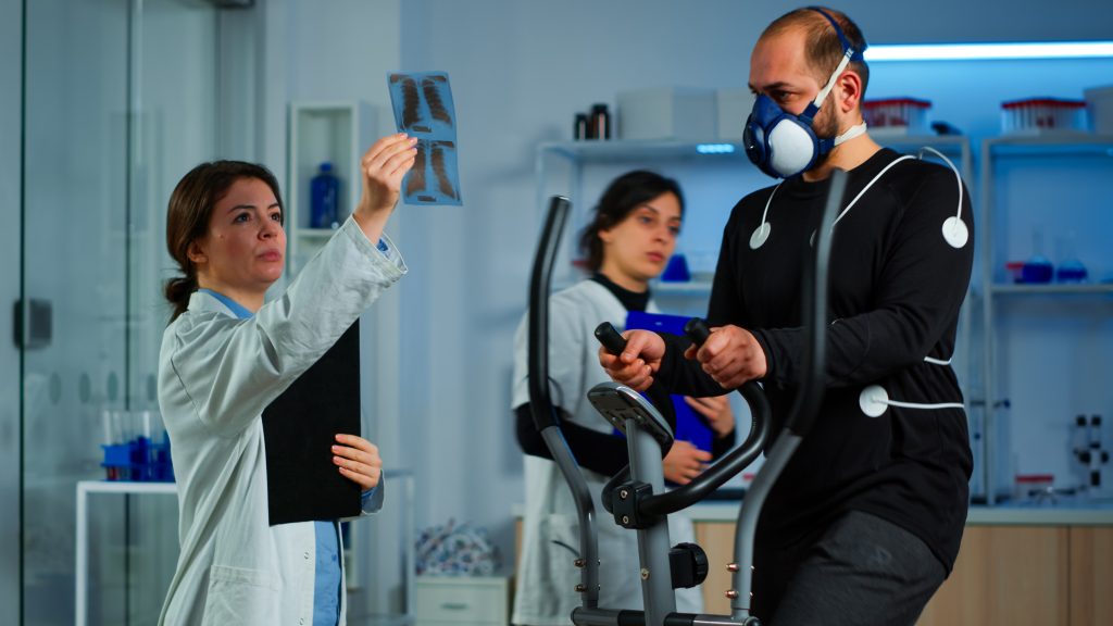 Physiotherapy Cost in Dhaka 5 team doctor researchers monitoring endurance man performance sports wearing mask running cross trainer 1 Physiotherapy Cost in Dhaka