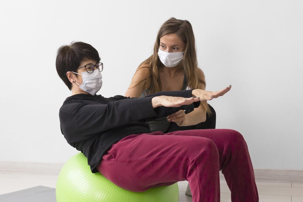 বাসায় ফিজিওথেরাপি নেওয়ার সহজ উপায় 3 woman training fitness ball while wearing medical mask 1 বাসায় ফিজিওথেরাপি নেওয়ার সহজ উপায়